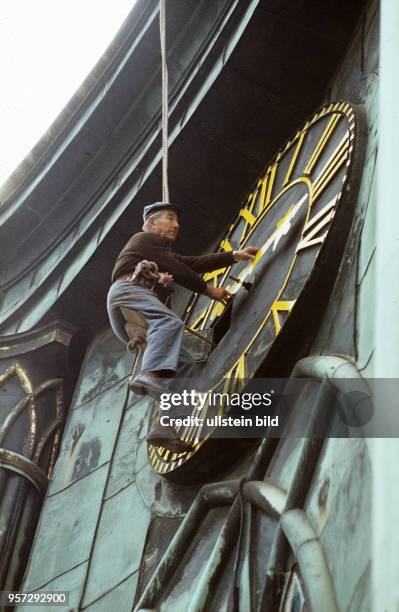 Ein Uhrmacher ausd der Werkstatt von Turmuhrmacher Liss in Ilsenburg hängt an einem Seil vor der großen histrorischen Turmuhr der Marienkirche und...