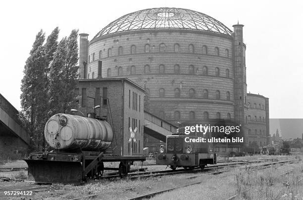 Ein abgestellter Waggon mit einem Kessel und eine kleine Rangierlok der Werksbahn vor einem Gasometer auf dem Gelände vom Gaswerk an der...