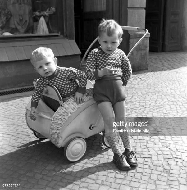 Zwei Jungen, ein Geschwisterpaar, an einem Korbkinderwagen vor einem Geschäft in Magdeburg, aufgenommen 1963.