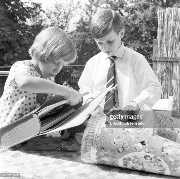 Ein Junge mit Krawatte und ein Mädchen schauen sich am Tag ihrer Einschulung ihre Schulranzen und ihre Schultüen an, undatiertes Foto von 1963.