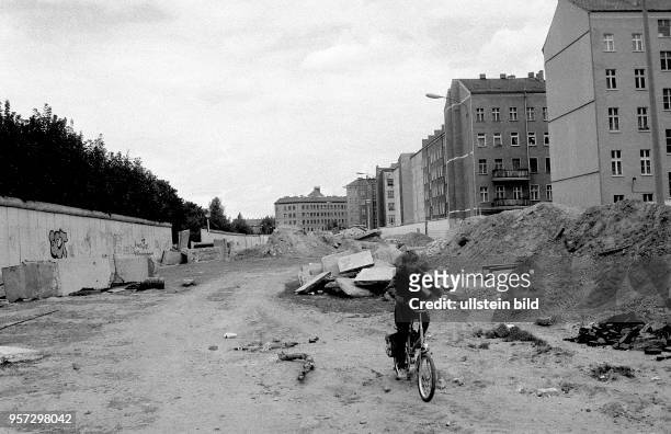 Ein Junge fährt mit seinem Fahrrad auf einen von Schutt und einer alten Baumwurzel bedeckten Grenzstreifen mit Mauerresten in der Nähe der Bernauer...