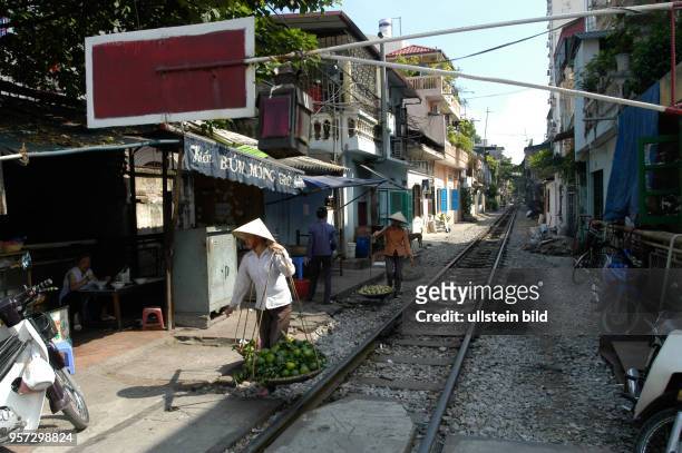 Zwei Straßenhändler laufen über das Schotterbett eines Gleises in einer engen Gasse in der Altstadt von Hanoi, der Hauptstadt der Sozialistischen...