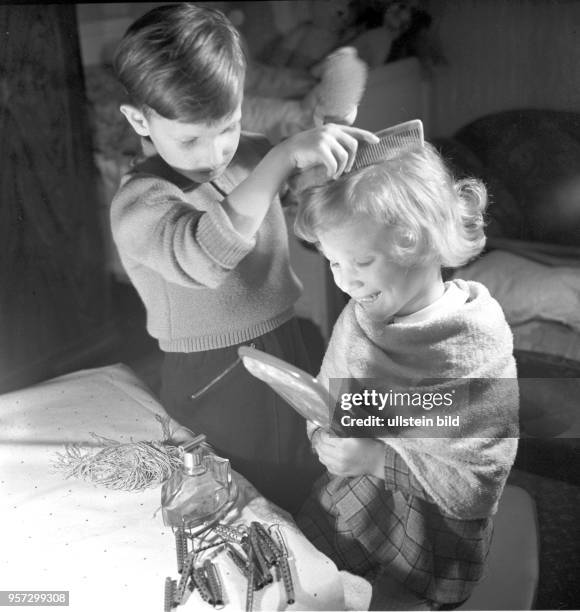 Zwei Kinder, ein Junge und ein Mädchen, spielen Friseur mit den dazugehörigen Utensilien, wie Kamm, Spiegel und Lockenwicklern, undatiertes Foto von...