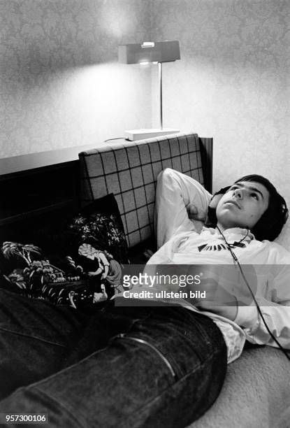 Ein Junge aus der 9. Klasse liegt auf dem Schlafsofa in seinem Zimmer und hört mit dem Kopfhörer Musik, aufgenommen 1986 in einer Neubauwohnung in...