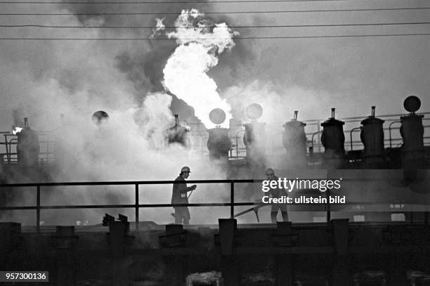 Flammen schlagen aus einem Kammerofen, zwei Arbeiter dichten umgeben von Abgasen mit Lehm und Flugasche die die Brennkammern ab, aufgenommen 1979 im...