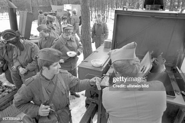 Soldaten der Nationalen Volksarmee im winterlichen Gelände bei der Verpflegung im Rahmen einer Übung, undatiertes Foto von 1981 bei Torgelow.