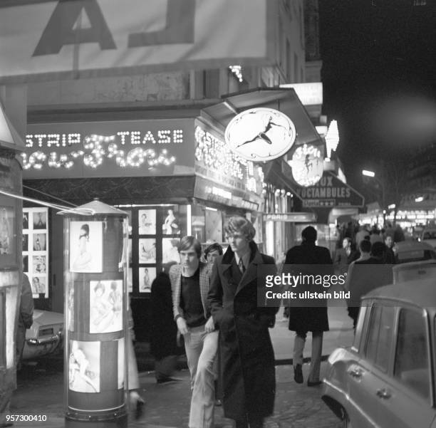 Junge Männer gehen am Abend an einem Striplokal im Rotlichtviertel von Paris vorbei, aufgenommen im November 1970.