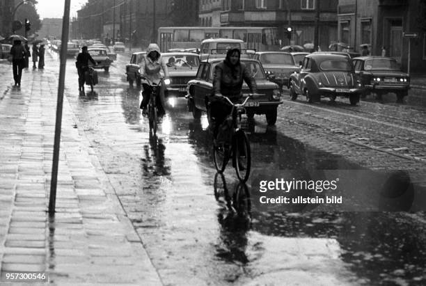 Radfahrer fahren neben Autos an der Kreuzung Karl-Liebknecht-Straße Ecke Bahnhofstraße in Cottbus durch den Regen, aufgenommen im August 1978. -
