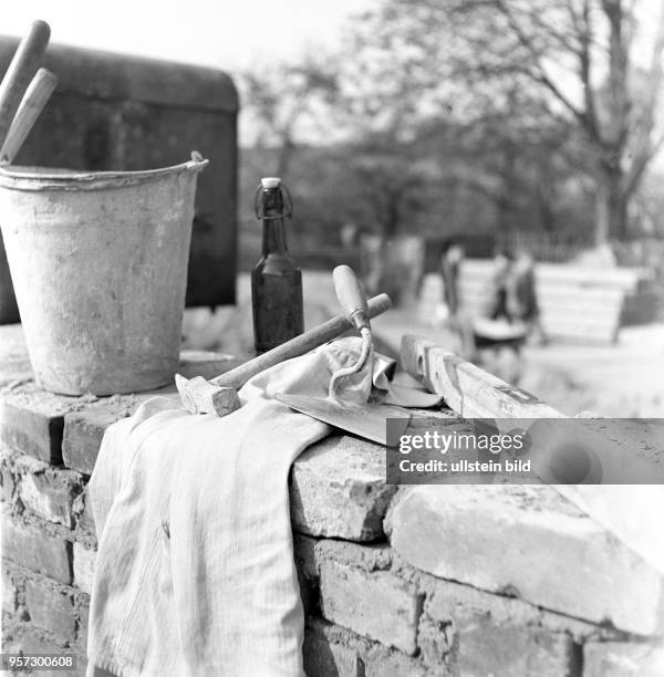 Utensilien und Handwerkszeug der Maurer - Eimer, Kelle, Hammer, Wasserwaage; Handtuch und eine Bierflasche - Stillleben auf einer Mauer auf einer...