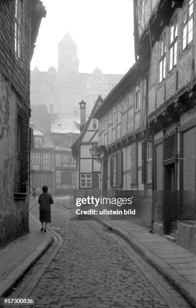 Eine Frau schlendert durch eine von Fachwerkhäusern gesäumte Gasse am Finkenherd in Quedlinburg, aufgenommen um 1960. Am Finkenherd soll der Sage...