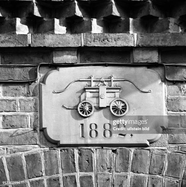 Ein Plakette an einer Hauswand in Güstrow zeigt eine Handpumpe als Symbol der Feuerwehr und die Jahreszahl 1882, undatiertes Foto von 1978.