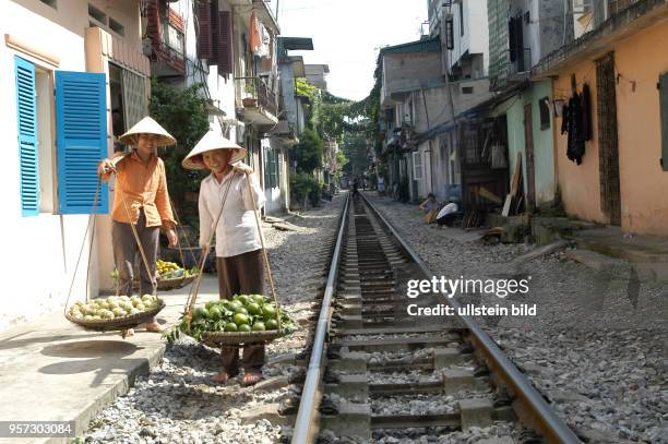 Zwei Straßenhändler stehen am Schotterbett eines Gleises in einer engen Gasse in der Altstadt von Hanoi, der Hauptstadt der Sozialistischen Republik...