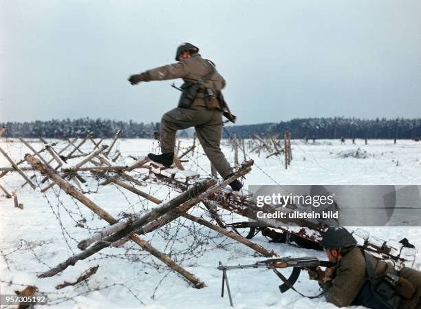 Infanteristen der Nationalen Volksarmee überwinden im winterlichen Gelände bei einer Übung ein Hindernis mit Stacheldraht, undatiertes Foto von 1981...