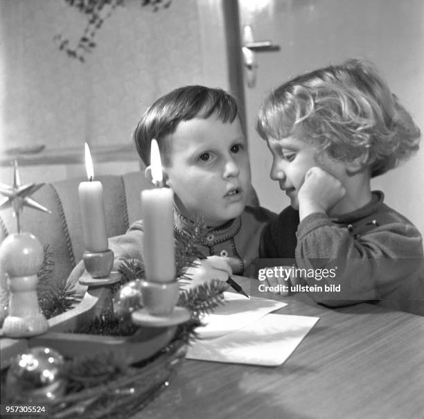 Ein kleines Mädchen und ein kleiner Junge mit einem Bleistift und Schreibpapier denken über ihre Wünsche an den Weihnachtsmann nach, undatiertes Foto...