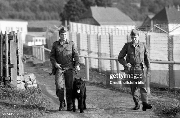 Zwei Grenzer der DDR-Grenztruppen gehen entlang der Grenzanlagen im thüringischen Dorf Wahlhausen mit einem Wachhund auf Patrouille, aufgenommen im...