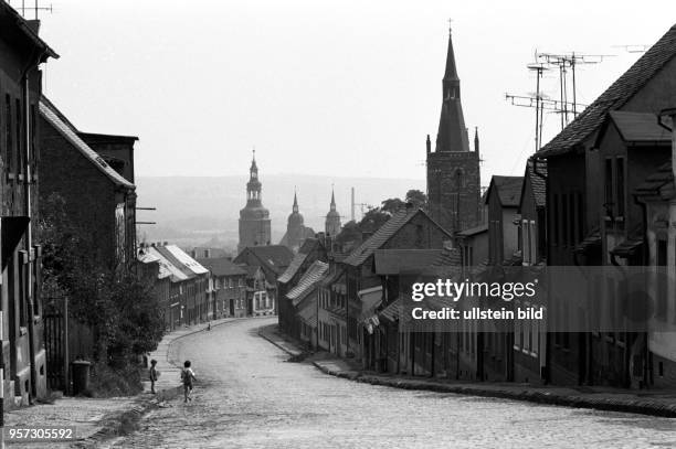 Kleine Häuser ducken sich an die abfallende Straße in der Lutherstadt Eisleben , aufgenommen im September 1978. Im Hintergrund ist die St....