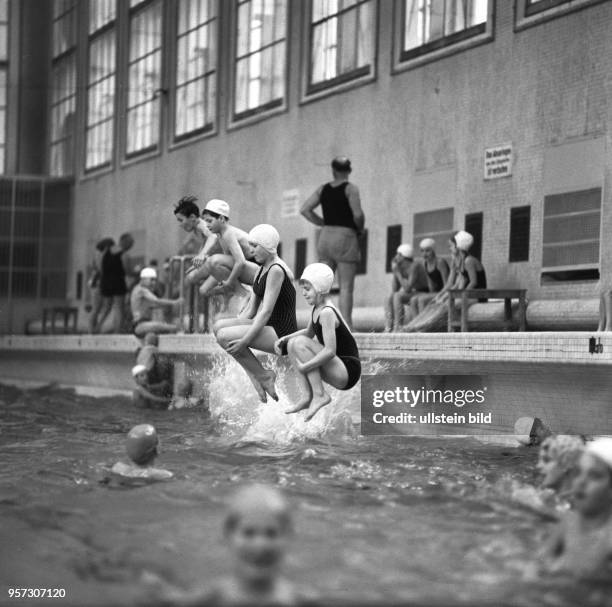 Besucher einer Schwimmhalle springen vom Beckenrand ins Wasser, aufgenommen 1976 in Berlin-Baumschulenweg.