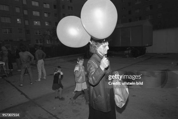 Eine Frau mit zwei Luftballons in der Hand und Kinder auf dem Heimweg von einem Straßenfest im Wohngebiet Ernst-Thälmann-Park in Berlin , aufgenommen...