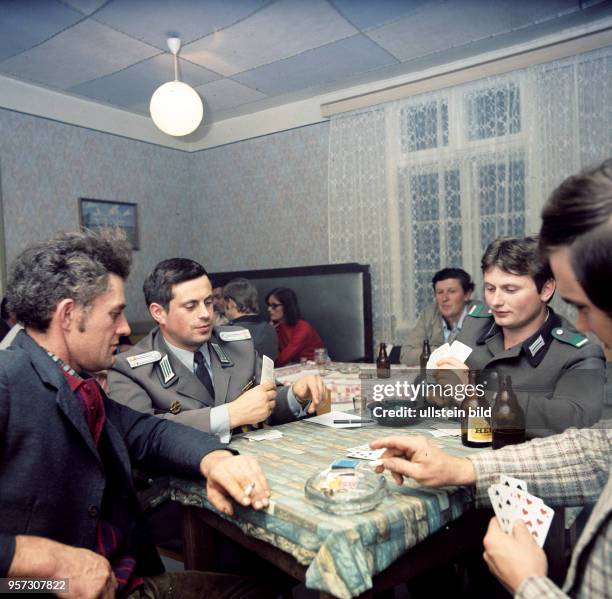 Ein Offizier und ein Soldat der DDR-Grenztruppen sitzen mit Einheimischen am Tisch einer Gaststätte in der Grenzgemeinde Wootz an der Elbe und...