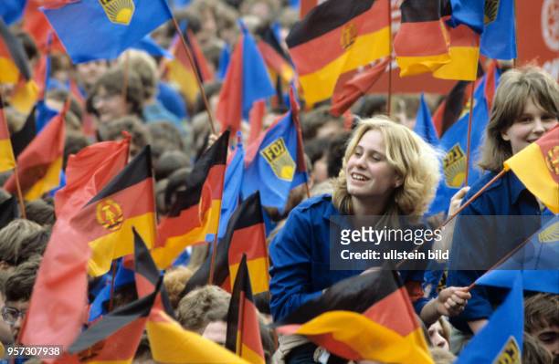 Eine blonde FDJlerin lacht über einem roten. Blauen und gelebn Fahnenmeer bei einer Veranstaltung im Rahmen des XI. Parteitages der SED im April 1986...