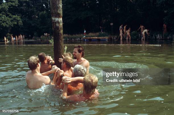 Männer transportieren einen Holzstamm im Wasser - Am Zeesener See in Senzig-Waldesruh liegt versteckt in waldreicher Gegend das über 60 Jahre alte...