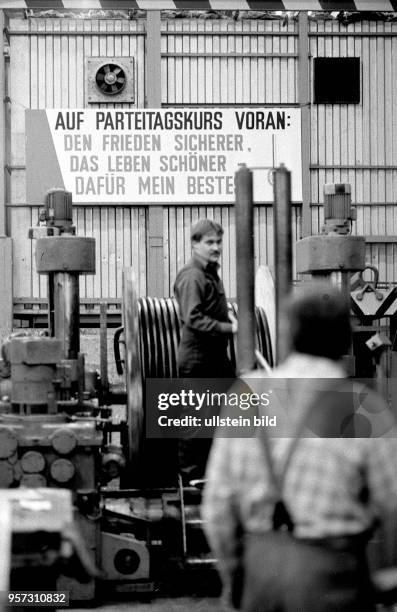 Im Kabelwerk Schwerin werden Kabel produziert, aufgenommen 1987. Im Hintergrund ist auf einem Schild die Losung zu lesen: "Auf Parteitagskurs voran:...