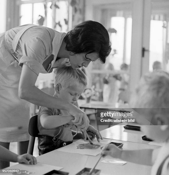 Eine Erzieherin hilft einem kleinen Jungen beim Malen mit einem Pinsel in einem Kindergarten Berlin-Treptow, aufgenommen im August 1968. Wilfried...
