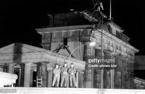 Soldaten der DDR-Grenztruppen stehen in der Nacht zum auf der Panzermauer am Brandenburger Tor in Berlin und verfolgen die nächtlichen...