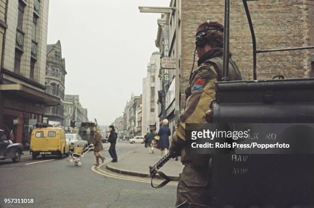 View of a British Army soldier wearing a maroon beret standing guard as residents visit shops and businesses in the centre of Belfast, Northern...
