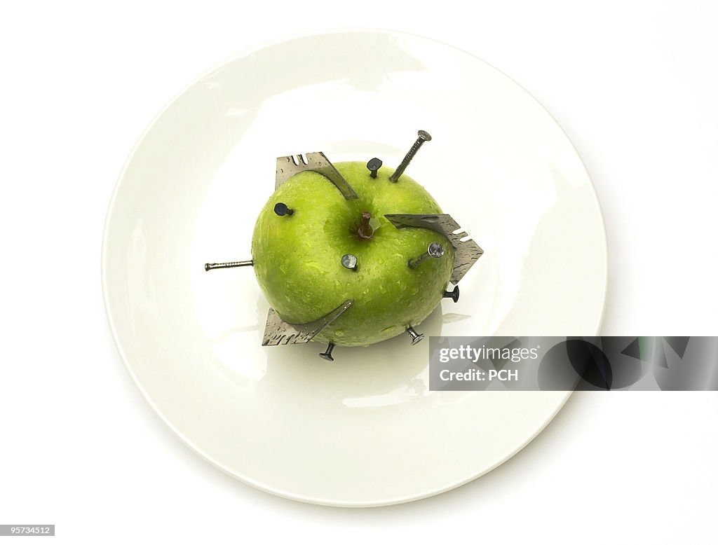 Green apple with razor blades and nails stuck in