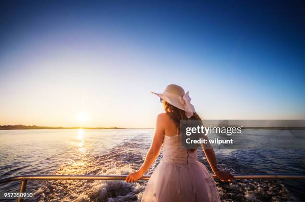 hintere ansicht junge frau auf dem rücken eines bootes bei sonnenuntergang - geländer stock-fotos und bilder