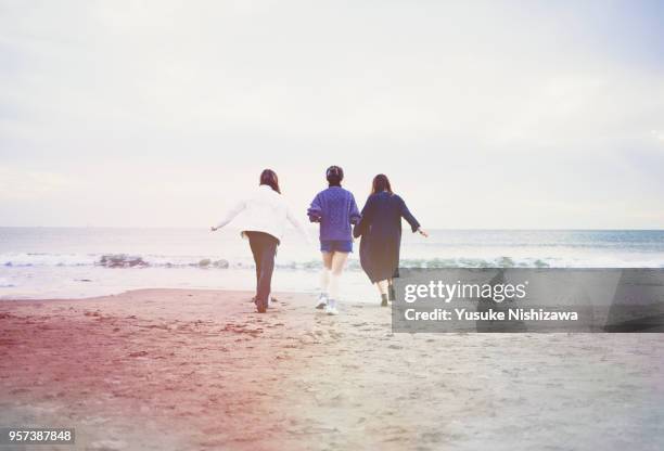 three young women walking together on sandy beach - three girls at beach stock pictures, royalty-free photos & images