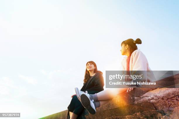 two young women sitting and talking - hochfrisur stock-fotos und bilder