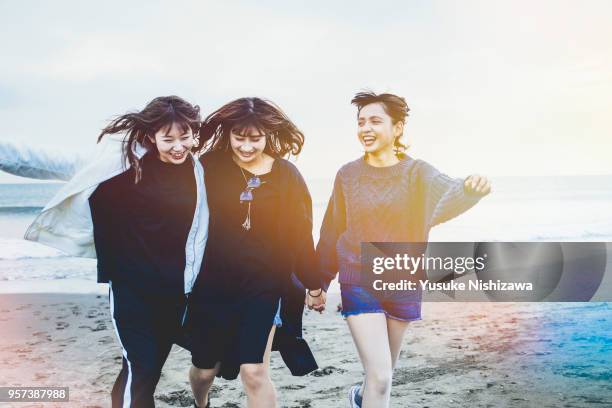 three young women walking together on sandy beach - japanese people fotografías e imágenes de stock