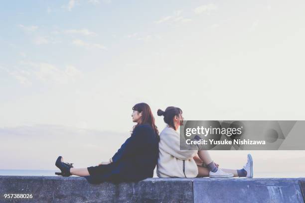 two young women sitting back to back - 日本人　女性　友達 ストックフォトと画像