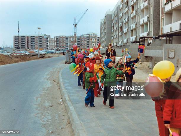 Kinder laufen mit kleinen bunten Papierfahnen und Luftballons auf einem Gehweg im Neubaugebiet Rostock-Schmarl, undatiertes Foto von 1978. Zwischen...