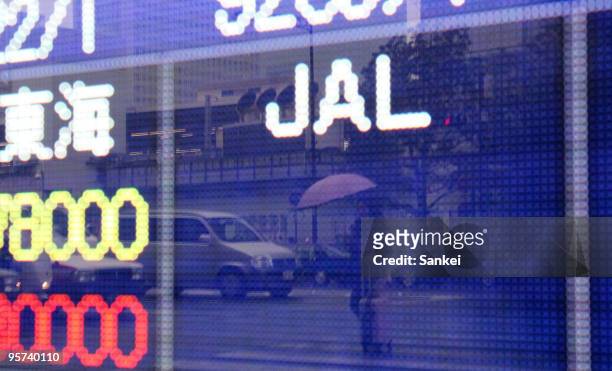 Pedestrian is reflected in an electronic board showing Japan Airlines Corp. 's share price, fell by the trading limit to 37 yen, outside a securities...