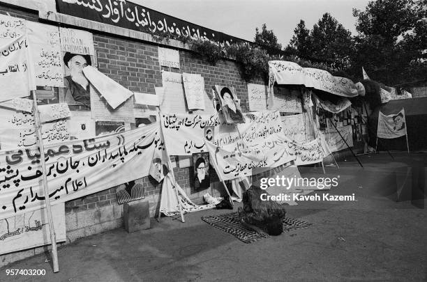 An Iranian revolutionary guard prays on a blanket spread on the pavement outside the US embassy walls in front of many banners with anti US and...