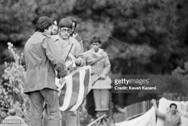 Standing on the walls of the compound, Iranian students following the Imam Khomeini line prepare to throw a US flag into the crowds gathering outside...