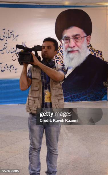 An Iranian cameraman stands in front of a banner with a photo of the supreme leader Ayatollah Ali Khamenei looking on while he shoots candidates...