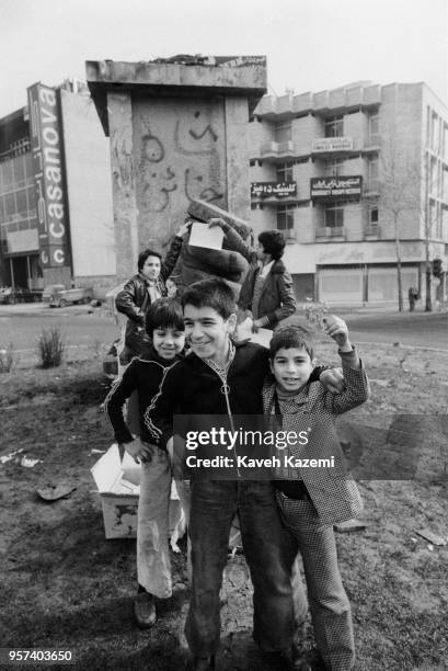 Group of boys appear in front of a monument with a missing statue with a slogan written "Shah the Traitor" in the late afternoon on the victory day...