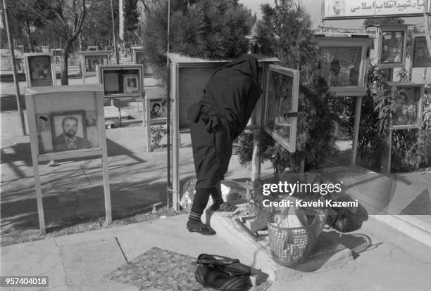Woman in black chador visits the tomb of her son fallen martyr in Iran-Iraq war an tidies up the metal casing where his photo is displayed in Behesht...