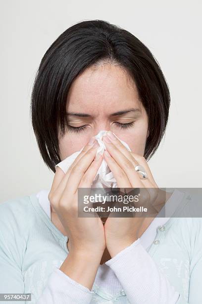 hispanic girl sneezing onto a tissue - closeup of a hispanic woman sneezing foto e immagini stock