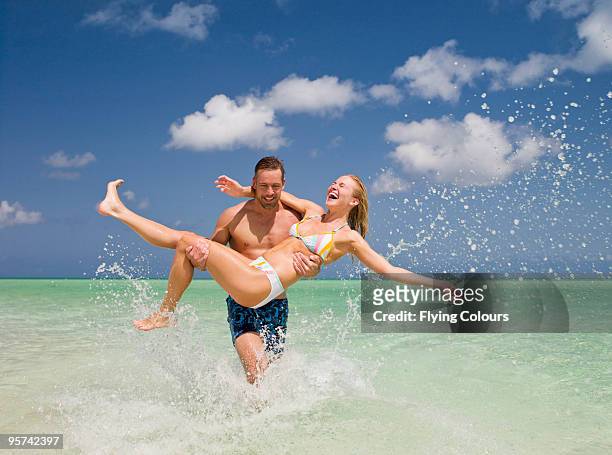 man carrying woman out of waves - couple and beach imagens e fotografias de stock