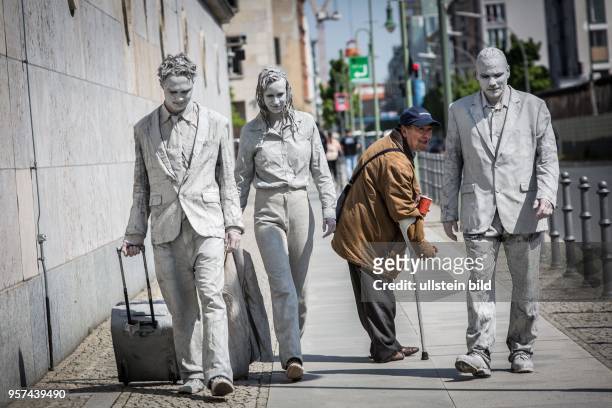 Deutschland Germany Berlin Drei in grau bemalte Menschen laufen an der Mauer des Finanzministeriums entlang. Ein Bettler, der ihre Wege kreuzt,...