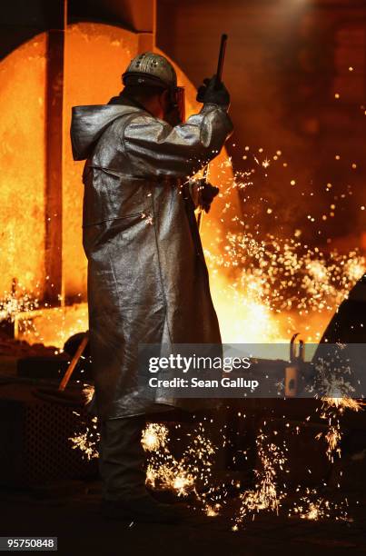 Worker wearing protective clothing takes a sample of molten iron heated to approximately 1480 degrees Celsius flowing from a blast furnace at the...