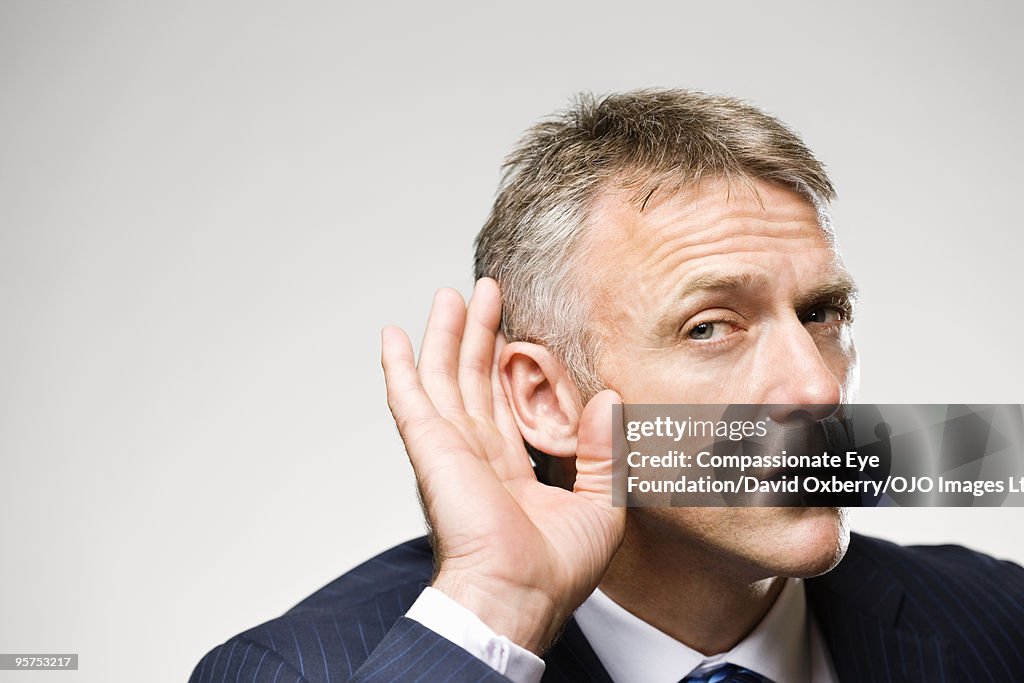 Man in suit cupping his ear with his hand