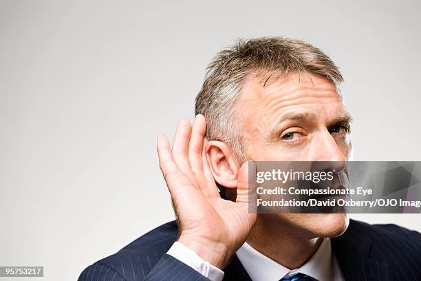 man in suit cupping his ear with his hand - problemas de comunicação imagens e fotografias de stock