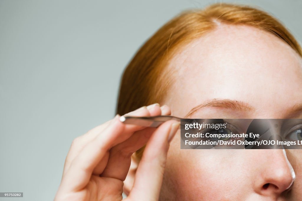 Close up of woman using tweezers on her eyebrow