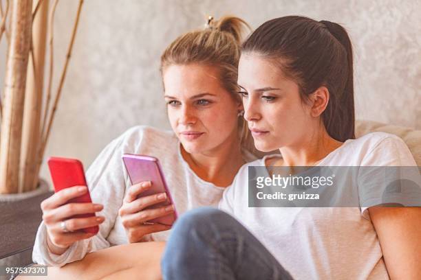 close-up of two female friends comparing their smartphones - phone comparison stock pictures, royalty-free photos & images